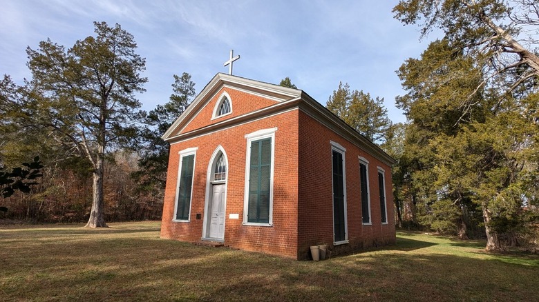 Grace Episcopal Church, a red brick building with a white cross on top surrounded by grass and trees