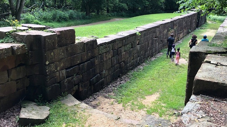 Family walking in an abandoned canal bed in Matildaville, with a stone wall surrounded by grass with trees in the background