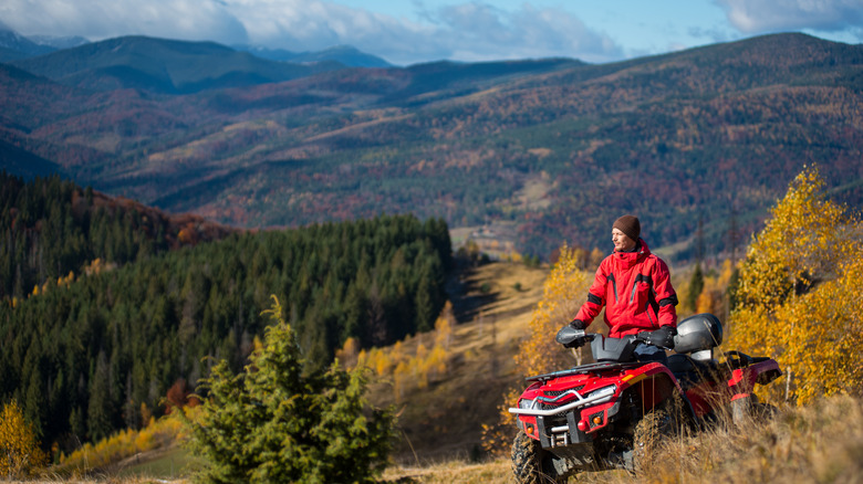 Man in red jacket on a red ATV looking out on the mountains in autumn