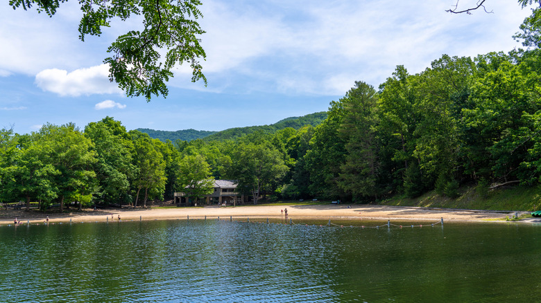 The lake and swimming beach dotted with people and surrounded by trees in Douthat State Park near Clifton Forge, VA