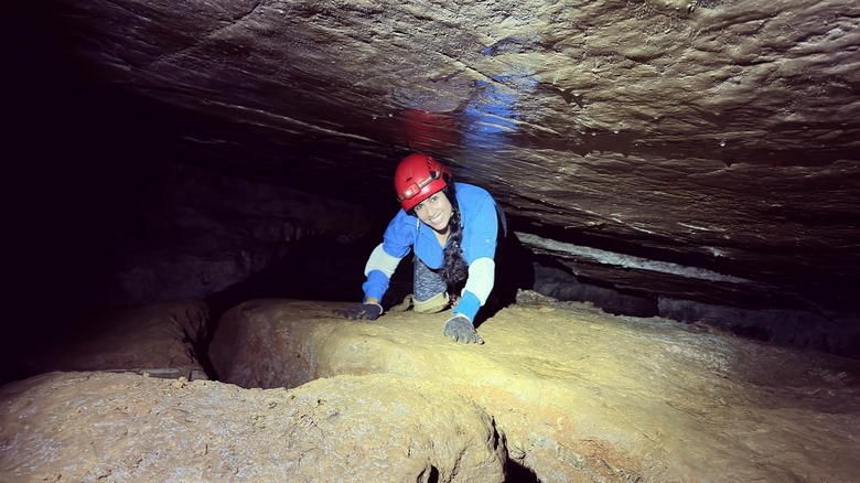 A smiling woman in caving gear climbs through a cave at Natural Tunnel State Park, in Virginia.