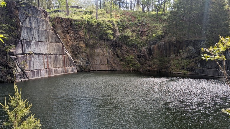 A view of lake water surrounded by soapstone walls and green foliage at the Quarry Gardens at Schuyler.