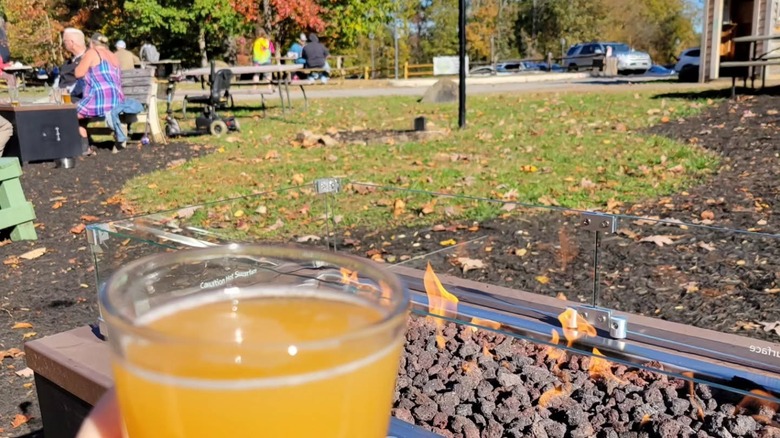 A hand a holding beer in front of a fire pit table