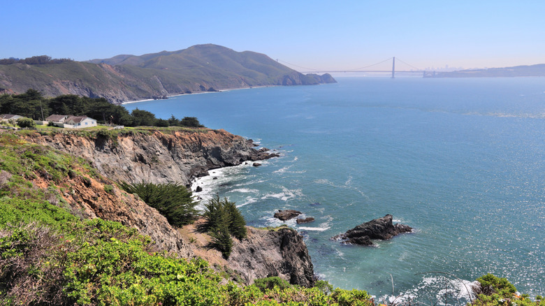 A rocky bluff looking down the the water of the San Francisco Bay with the Golden Gate Bridge and city skyline in the distance.