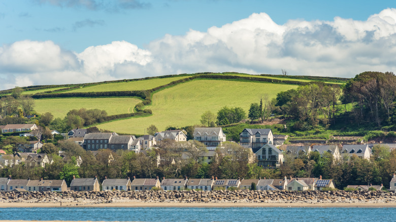 A panoramic view of buildings, water, and a grassy, tree-studded hillside in Llansteffan, Wales