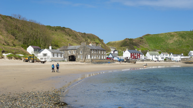 Two walkers stroll the beach as washes the sands at Porthdinllaen