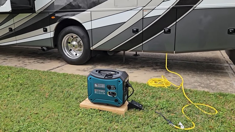 Teal Konner & Sohnen generator on green grass in front of a black and white RV, connected by a yellow cable