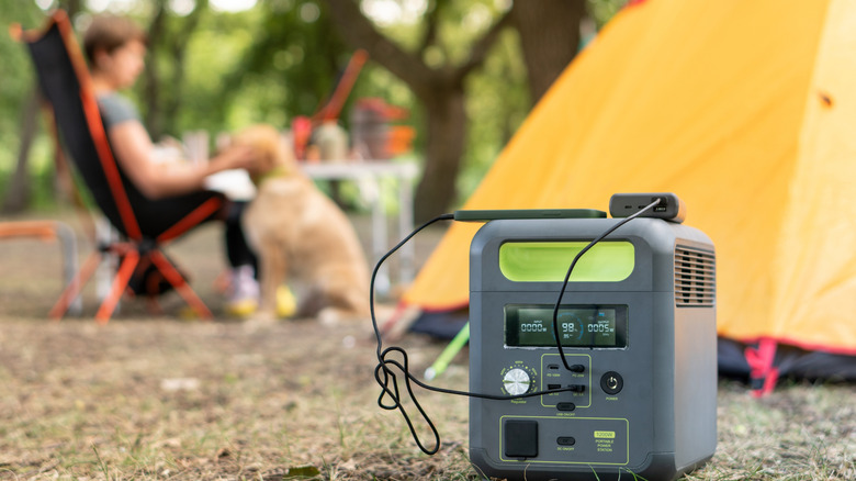 Gray power station in the foreground, with a yellow tent, dog, and man sitting in a camp chair blurry in the background