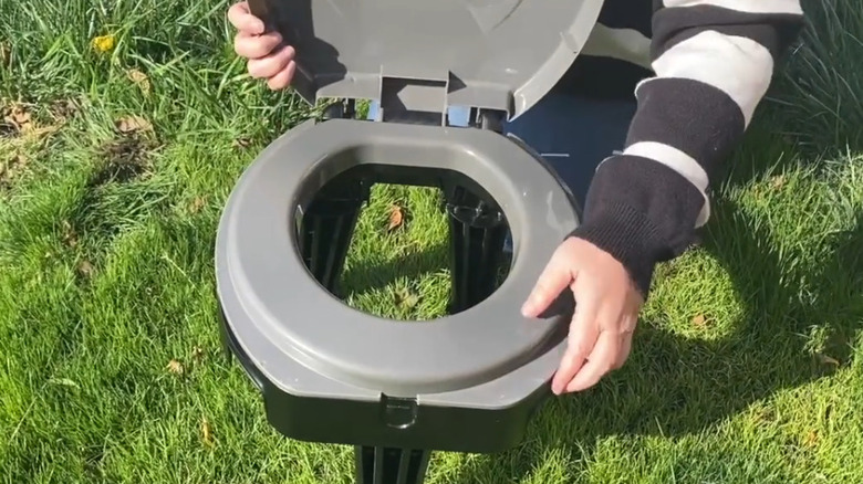 A portable camping toilet being set up outdoors on grass