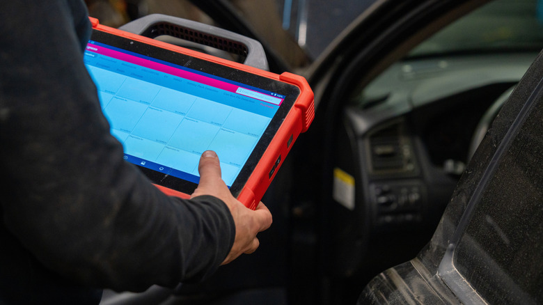Person checking vehicle holding diagnostic reader
