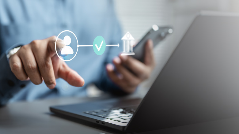 Person holding phone, laptop on desk, and pointing at graphic on screen of person, checkmark and bank