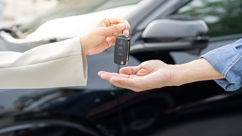 Someone handing another person a car key fob standing in front of a vehicle