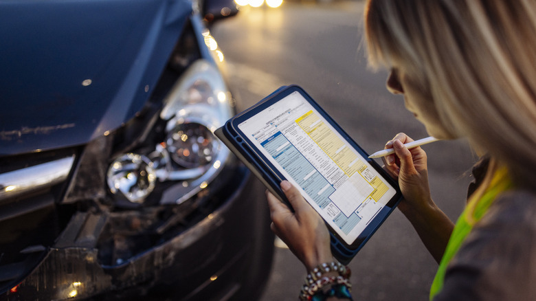 Woman looking at report form and vehicle damage after accident