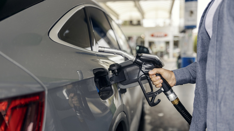Person pumping gas into a car, holding the fuel nozzle