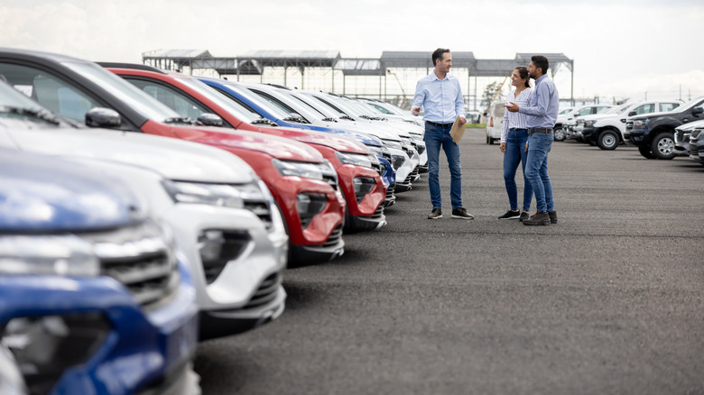 People walking in a lot of vehicles with a sales rep