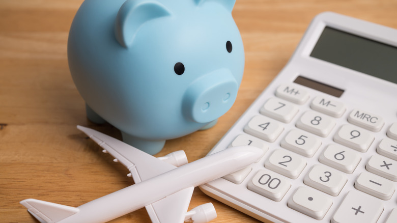 A calculator, piggy bank, and airplane model representing the costs of travel