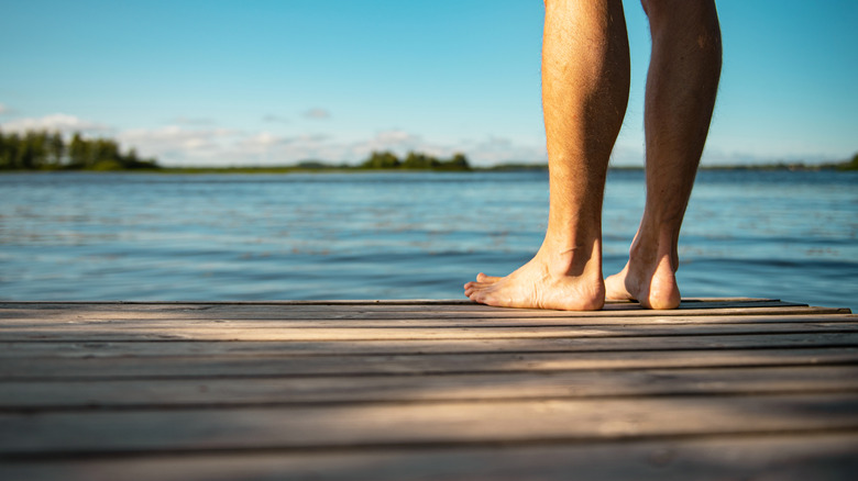 A shot of a person's feet and lower legs standing on a dock on a lake