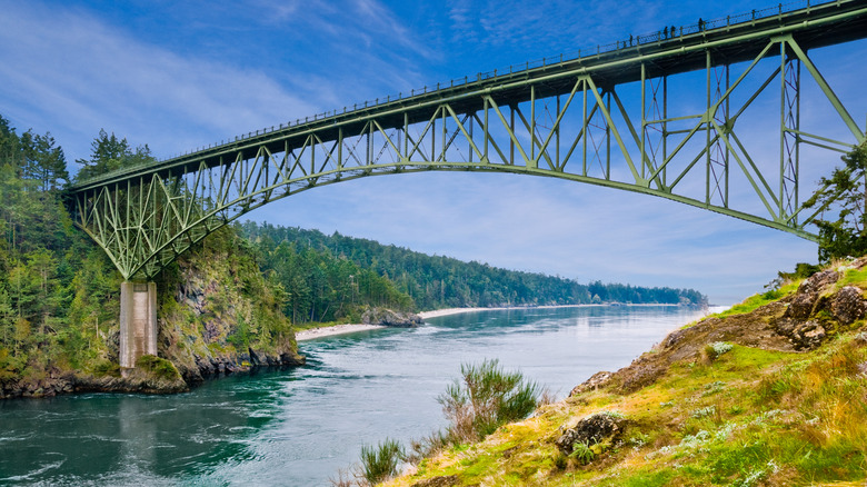 Green truss bridge spanning two forested shores over green waters of Deception Pass Washington