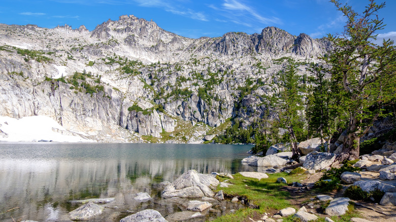 An alpine lake sits below rocky peaks dotted with green trees