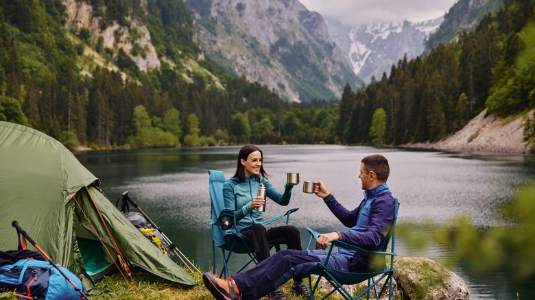 A couple of campers by the lakeside with mountains in background