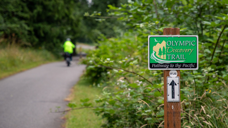 A bicyclist cruises past a green sign marking the Olympic Discovery Trail near Sequim Bay State Park, Washington.