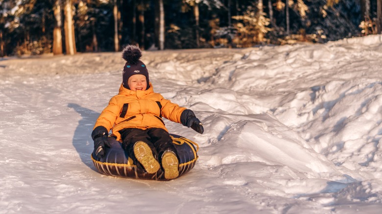 Toddler wearing a yellow jacket sliding down a hill on a snow tube