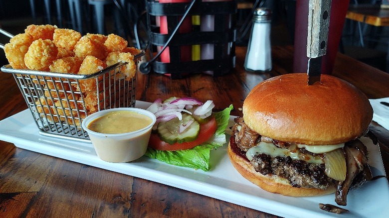 A juicy burger paired with salad, tater tots, and dipping sauce on a plate at Whiskey Gulch.