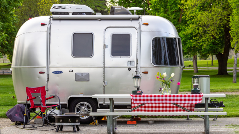 A small Airstream trailer parked at a Bridgeport State Park campsite with grass and trees in the background and a picnic table and camping stuff in the foreground.