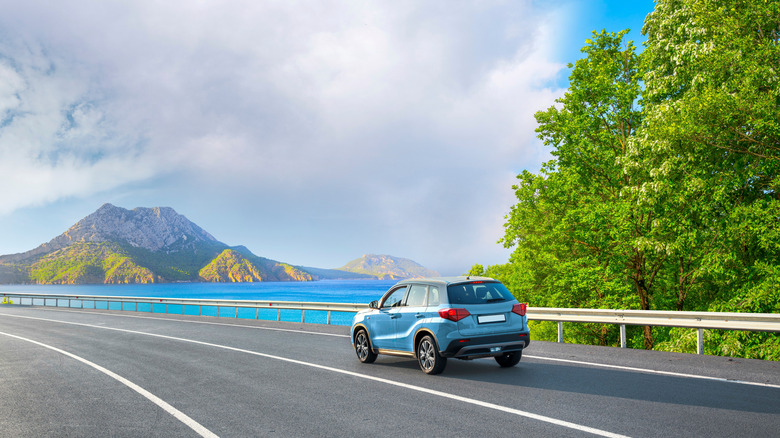 a blue car on a scenic coastal road with bright blue waters and green mountains on a clear day