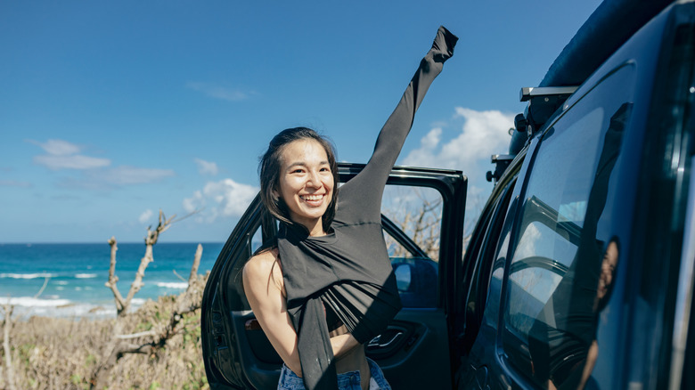 a woman changing clothes by her car parked by the beach