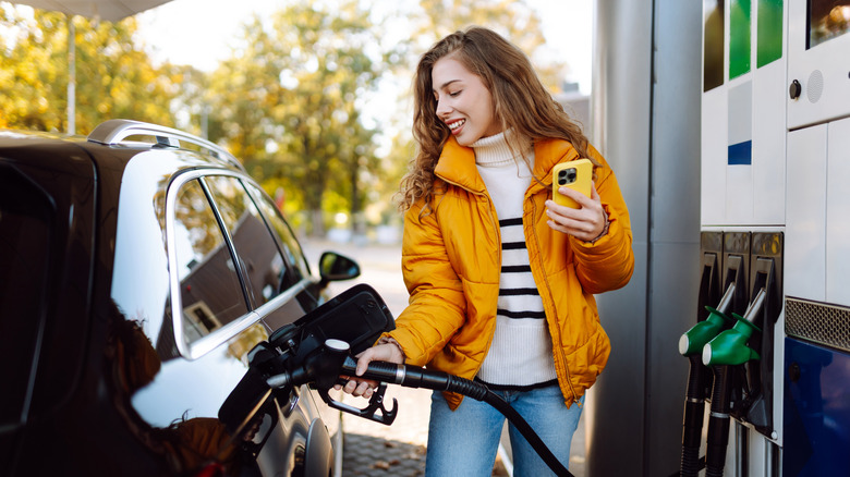 a young woman fills her tank at a gas station