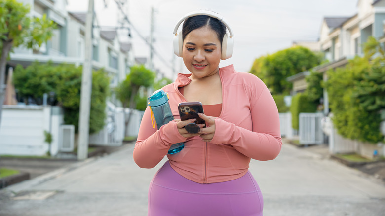 A woman in athletic clothing walks down the street, looking at her phone