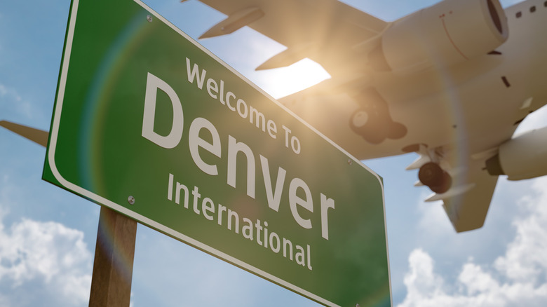 an airplane flies over a sign saying, welcome to denver international
