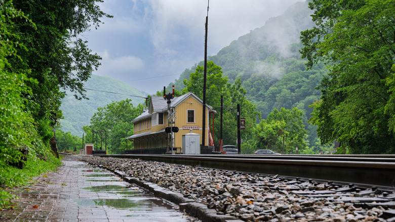 Yellow train depot surrounded by greenery and behind railroad tracks