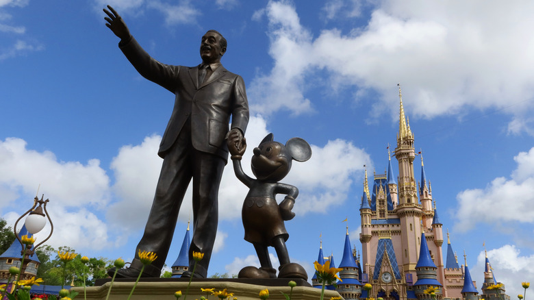 A statue of Walk Disney holding hands with Mickey Mouse stands in a garden in front of Cinderella's Castle at Disney World's Magic Kingdom Park in Orlando, Florida