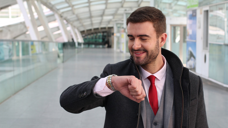 Man in an airport looking at his wrist watch smiling