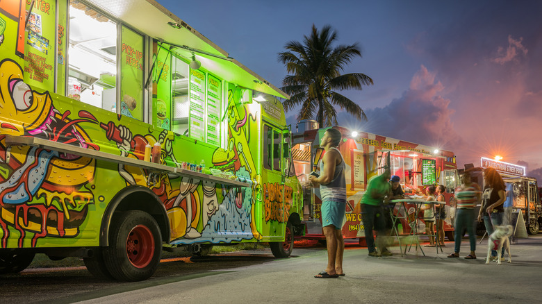 A row of Miami Beach food trucks at sunset while a man looks at the menu