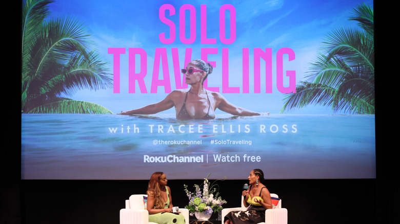 Actress Tracee Ellis Ross being interviewed by a woman in front of a promotional image for Ross's TV show Solo Traveling