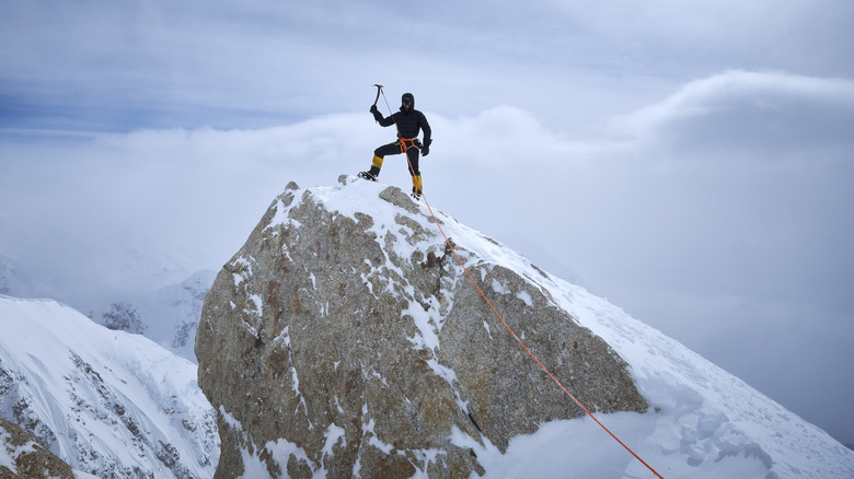 A mountaineer stands amongst the clouds in Denali National Park while holding an ice axe