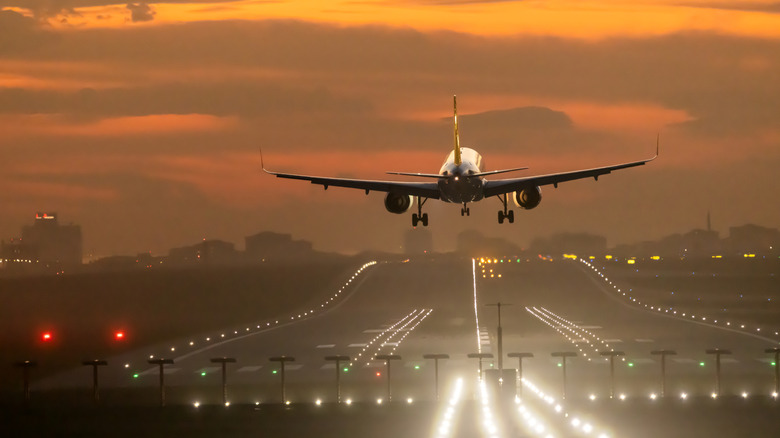 A commercial airliner takes off in the afterflow of sunset with the runway lit up below
