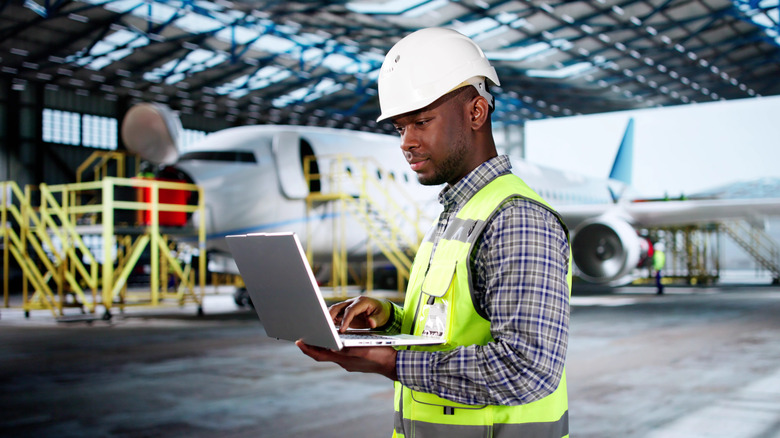 Man in a high-vis vest and helmet in a hanger, alongside a plane.
