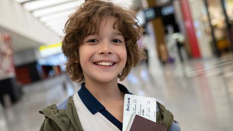 Smiling boy holding his passport and plane ticket at an airport.