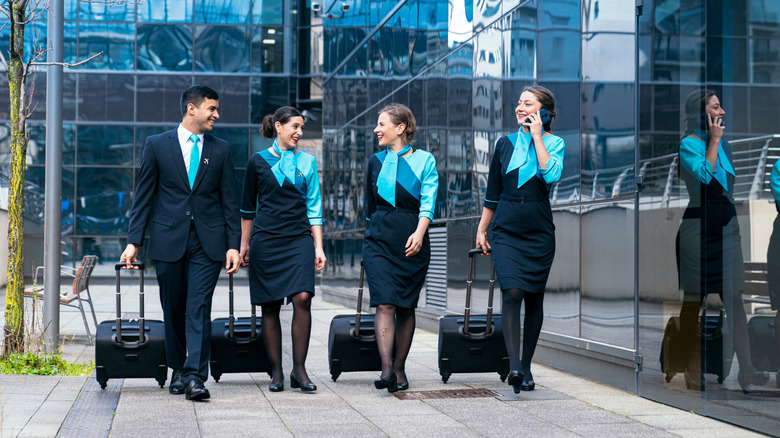 A group of flight attendants walk to their next destination rolling luggage behind them
