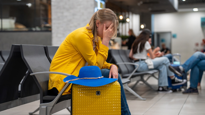 woman holds face and looks upset in airport