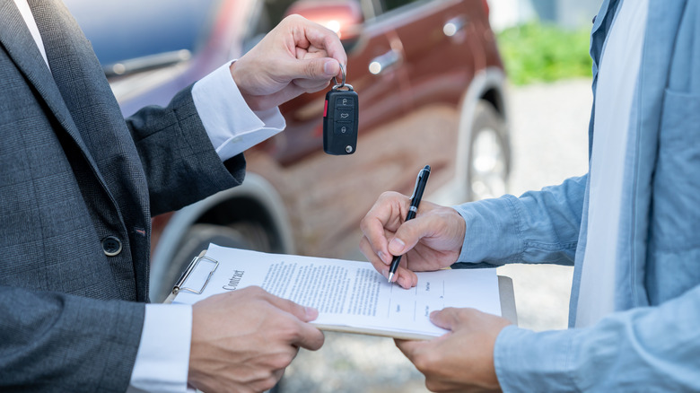 Someone handing over car keys while another is signing a contract