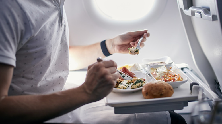 Male passenger eating an airline meal of pasta, chicken, and bread