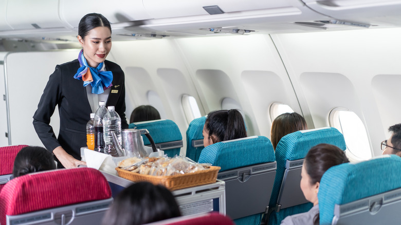 A flight attendant pushing a cart of snacks down an airplane aisle