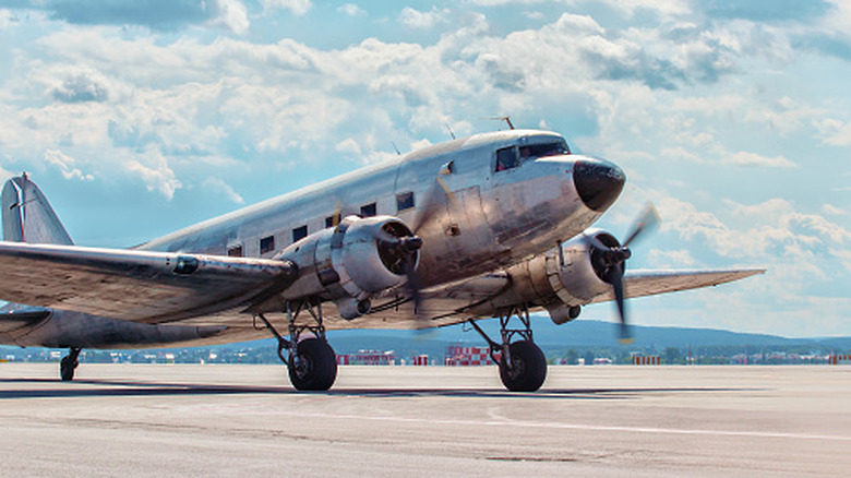 An old plane spins its propellers on the tarmac of a sun-bleached airfield