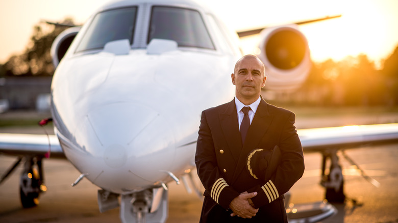 Pilot holding his cap in front of a plane at sunset