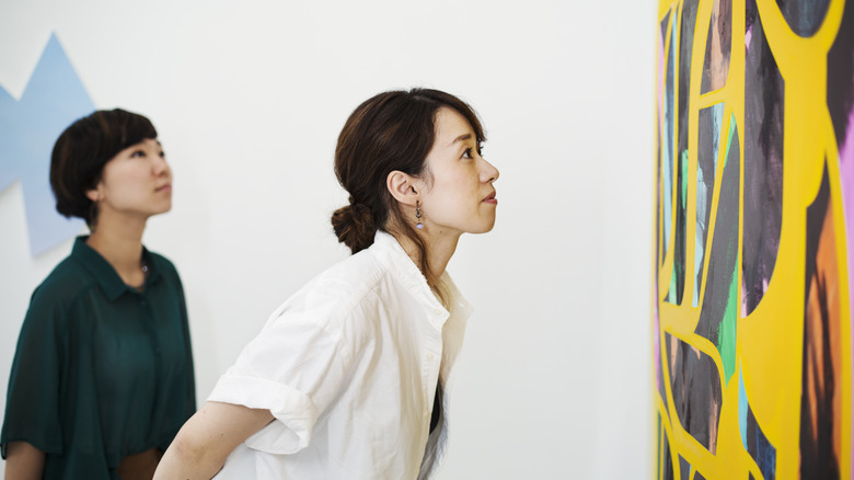 A woman looks closely at an abstract work of art, bending over at the waist to see it more closely